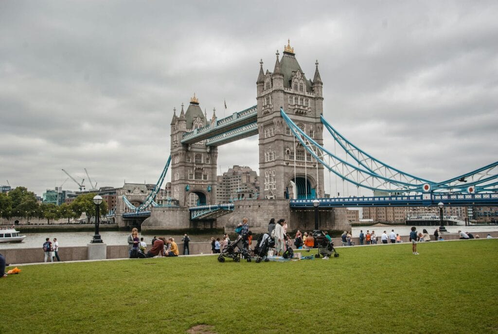 Iconic Tower Bridge in London with people enjoying a park view on a cloudy day.